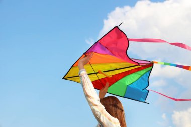 Güneşli bir günde mavi gökyüzünde uçurtma uçuran genç bir kadın.