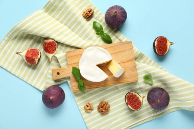 Lezzetli Camembert peyniri, taze incir ve mavi arka planda fesleğen yaprakları.