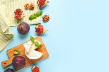 Lezzetli Camembert peyniri, taze incir ve mavi arka planda fesleğen yaprakları.