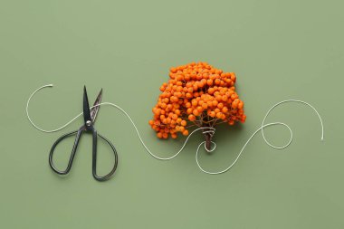 Yeşil arka planda makas, iplik ve olgun yaban mersini dallarıyla kompozisyon