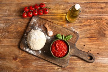 Lezzetli domates sosu, çiğ hamur ve ahşap arka planda malzemelerle dolu bir pano.