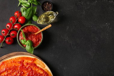 Pizza için çiğ hamurlu pano ve siyah grunge arka planında bir kase lezzetli domates sosu, yakın plan.