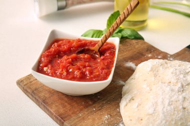 Lezzetli domates sosu ve beyaz grunge arka planında çiğ hamur olan tahta, yakın plan.