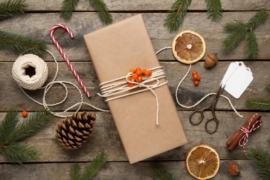 İp, makas, köknar ağacı dalları, kurutulmuş portakal dilimleri ve ahşap zemin üzerinde yabanmersini dolu Noel hediyesi kutusu.