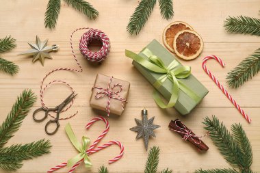 İp, makas, kurutulmuş portakal dilimleri, köknar ağacı dalları ve ahşap arka planda dekoru olan Noel hediyesi kutuları.