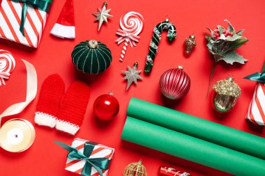 Farklı Noel süslemeleri, hediye kutuları ve kırmızı arka planda paketleme malzemeleriyle güzel bir kompozisyon