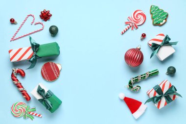 Hediye kutularından yapılmış çerçeve, Noel topları, kurabiyeler ve mavi arka planda şeker kamışları