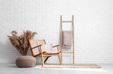 Stil hasır puf, rahat koltuk ve beyaz tuğla duvarın yanındaki tahta merdiven.