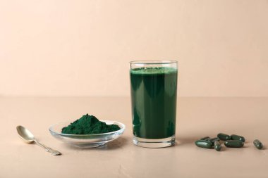 Bir bardak taze spirulina içeceği, haplar ve bej arka planda bir kase toz.
