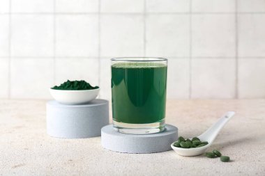 Bir bardak taze spirulina iç ve bej grunge masasında haplarla kepçele, yakın plan.