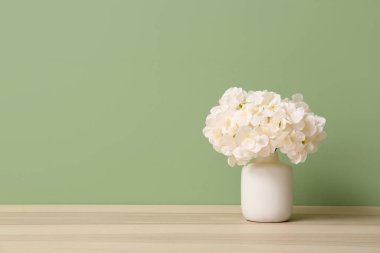 Yeşil duvarın yanındaki masada yapay çiçekli vazo.