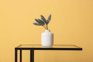 Sarı duvarın yanındaki masada yapay çiçekli vazo.