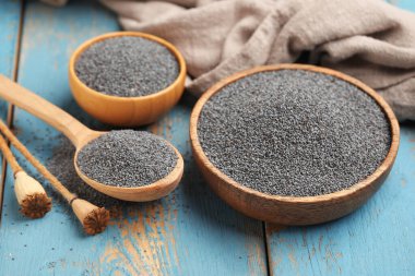 Mavi ahşap arka planda haşhaş tohumlu kaseler ve kaşıklar, yakın plan.