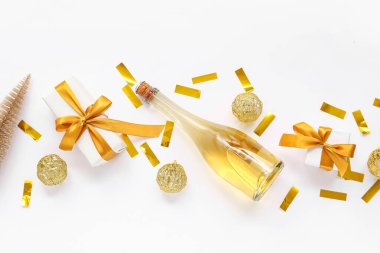 Altın Noel topları, konfeti, bir şişe şampanya ve beyaz arka planda hediye kutuları.