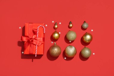 Composition with golden Christmas balls, gift box and confetti on red background