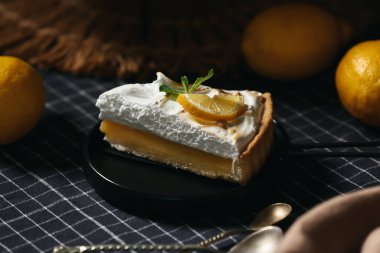 Plate with piece of tasty lemon pie on black napkin as background, closeup