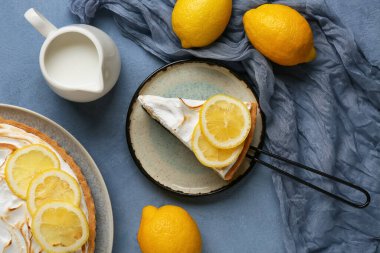 Plate with piece of tasty lemon pie and jug of milk on blue grunge background, closeup