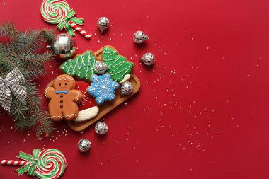 Disko topları, köknar ağacı dalları ve kırmızı arka planda Noel kurabiyeleri olan kompozisyon