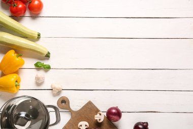 Beyaz ahşap arka planda farklı sebzelerle tencere yapmak.