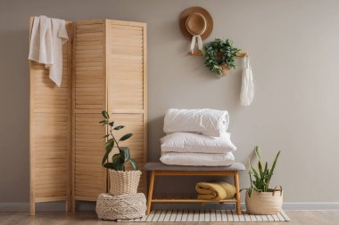 Oturma odasındaki gri duvarın yanında çekmeceler, yastıklar ve battaniyeler var.