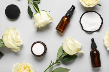 Güzel beyaz gül çiçekleri ve kozmetik krem kavanozu ve gri arka planda gerekli yağ şişeleri.