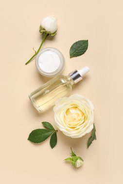 Beautiful white rose flowers with jar of cosmetic cream and bottle of essential oil on beige background