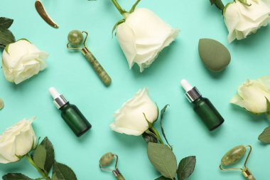 Beautiful white rose flowers with jade rollers, makeup sponge and bottles of cosmetic oil on turquoise background