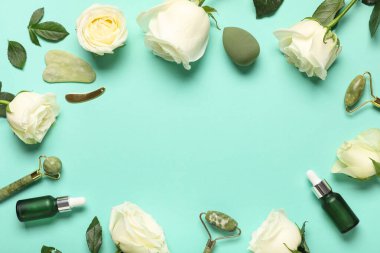 Frame made of beautiful white rose flowers with face massage tools and makeup sponge on turquoise background