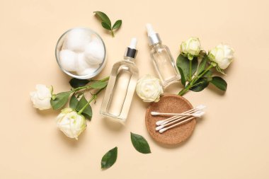 Kozmetik ürün şişeleri, pamuklu bezler ve bej arka planda yün topları olan güzel beyaz güller.