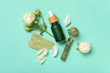 Kozmetik ürünlerle dolu güzel beyaz güller masaj silindiri ve turkuaz arka planda guasha.
