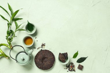 Yeşil arka planda kuru ütülenmiş puer çayı, çaydanlık ve fincanla kompozisyon