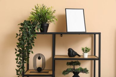 Suni bitkilere sahip raf ünitesi, bej duvarın yanında boş çerçeve ve dekor