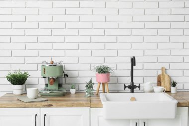 Kahve makinesi ve yapay bitkilerle lavabo mutfaktaki beyaz tuğla duvarın yanında.