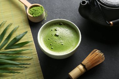 Siyah grunge arka planda bir kase kibrit çayı ve tropikal yaprak kompozisyonu, yakın plan.