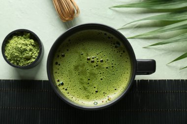 Hasır hasırlı kompozisyon, bir kase lezzetli kibrit çayı ve yeşil grunge arka planda tropikal yaprak, yakın plan