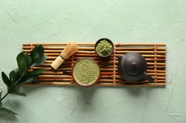 Bambu hasırlı kompozisyon, bir kase kibrit çayı ve yeşil grunge arka planda çaydanlık.