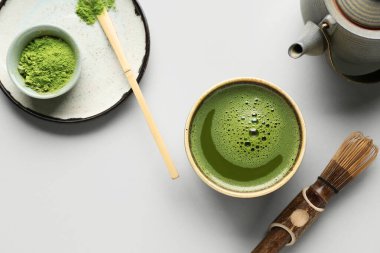 Bir kase taze kibrit çayı, toz, chasen, chashaku ve gri arkaplanda çaydanlık.