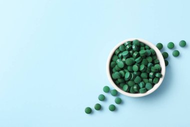 Mavi arka planda bir kase spirulina tableti.