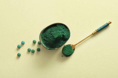 Yeşil arka planda bir kase spirulina tozu tablet ve kaşık.