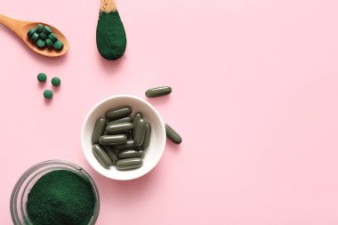 Bir kase spirulina kapsülü ve pembe arka planda kaşık dolu toz.