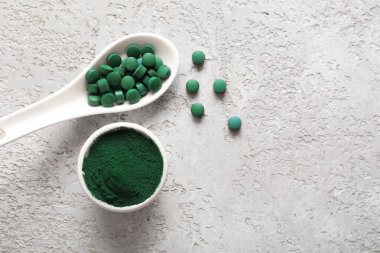 Bowl of spirulina powder with spoon and tablets on grey grunge background