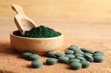 Tabletli bir kase spirulina tozu ve ahşap arka planda kepçe.