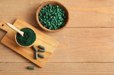 Tahta arka planda kapsülleri olan spirulina tozu ve tabletler.