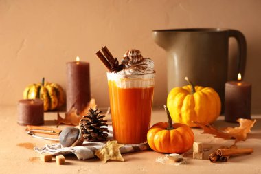 Bir bardak portakal kabaklı latte, krem şanti ve bej arka planda yanan mumlar.