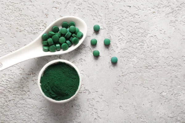 Bir kase spirulina tozu ve gri grunge arka planda kaşık ve tabletler.