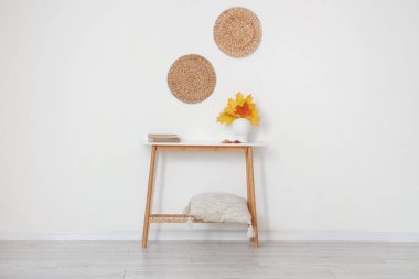 Sonbahar yapraklı vazo ve kitaplarla aydınlık duvarın yanındaki odada.