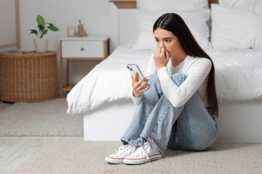 Yatak odasında cep telefonu kullanan korkmuş genç bir kadın.