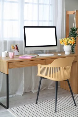 Pencerenin yanında modern bilgisayar ve narsisli çiçeklerle rahat bir iş yeri