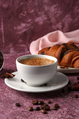 Kahve çekirdekli bir fincan nefis espresso ve mor arka planda kruvasan.