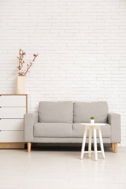 Oturma odasının içinde kanepe, çekmeceler ve beyaz tuğla duvarın yanındaki masa.